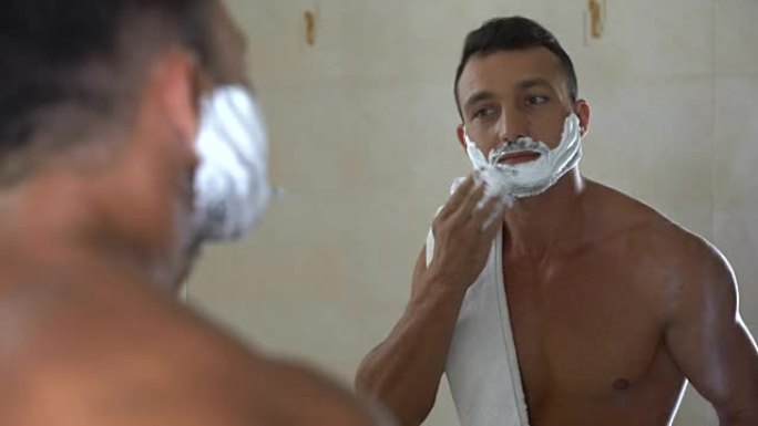 残忍的男性展示剃须刀，并将剃须膏涂抹在脸部和胡须上