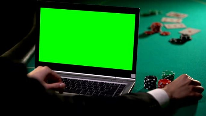 男性赌徒在笔记本电脑上在线赌扑克，拿着幸运的骰子，绿色屏幕