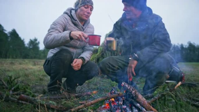 男人和女人在火炉旁喝茶，他们在森林空地上点燃