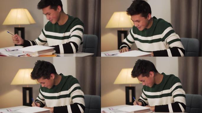 微笑的亚洲男孩在工作簿中写作和看书本的特写侧视图。快乐的青少年学生晚上在室内学习。教育，快乐，生活方