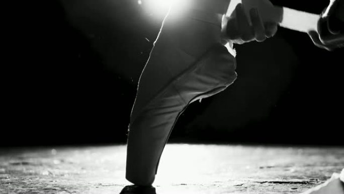 一只女性的手在腿上绑着脚尖鞋的特写镜头，在黑色背景上的聚光灯下隔离。