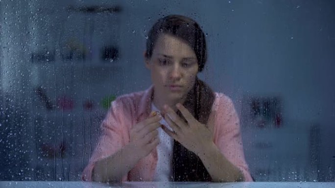 女人在下雨的窗户后面脱下订婚戒指，分手后心烦意乱