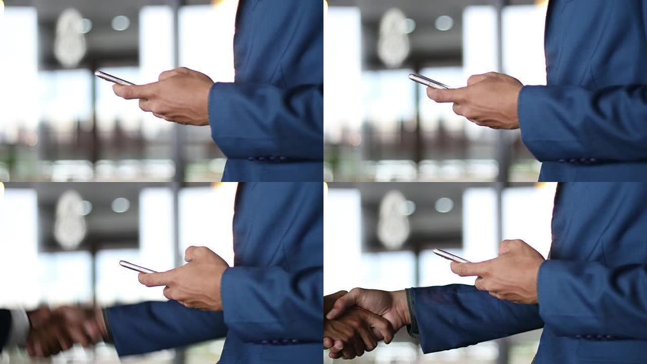商务握手两名商人握手并使用智能手机