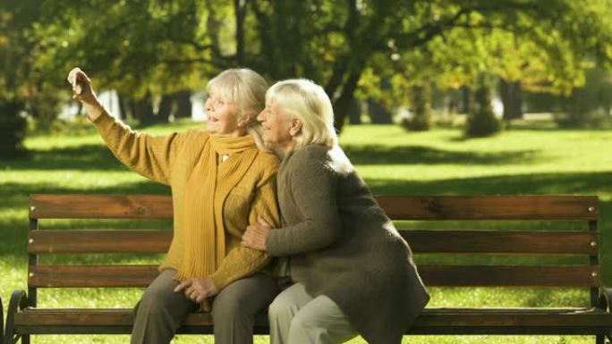 两名老太太在手机上自拍坐在公园科技的长凳上