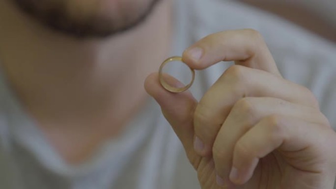 坐在家里的没有被认出的大胡子男人拿着金色结婚戒指的肖像。
