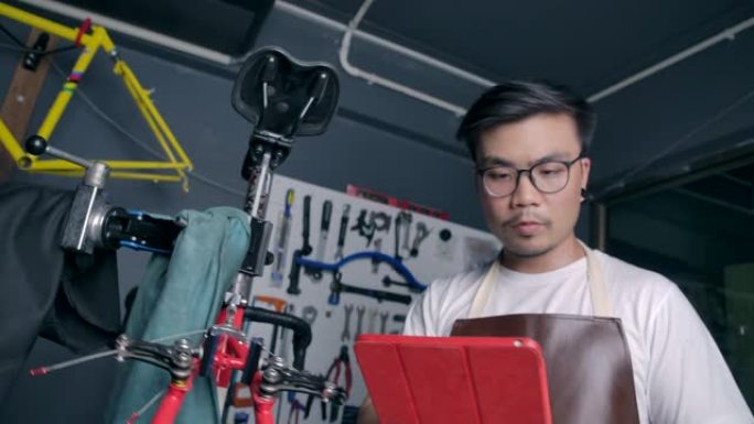 4k慢动作亚洲男子戴眼镜他是一家自行车店的老板。是一家小企业，他正在修理自行车并旋转车轮。检查条件，
