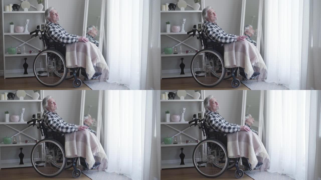 坐在轮椅上思考的成熟白人白发男子的侧视图。孤独的老人独自在家度过一天。老人，退休，残疾人。