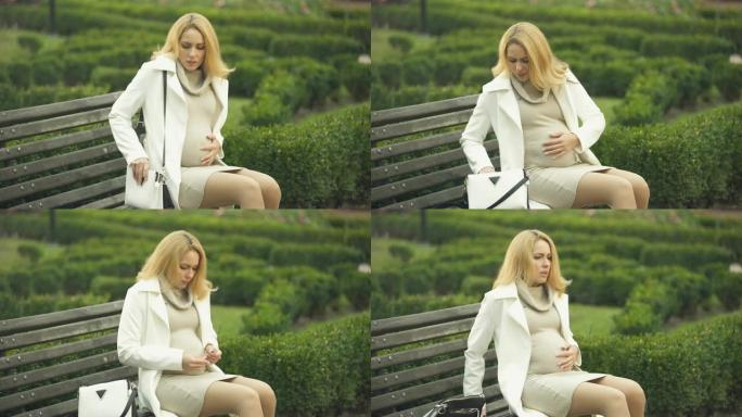 怀孕的金发女人吃药，坐在公园长椅上，感觉腹痛