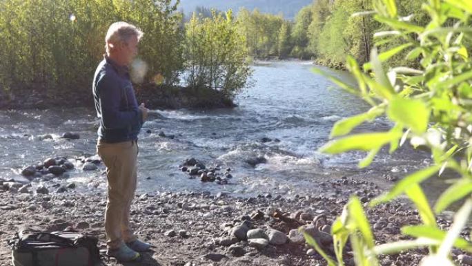 成熟的男性徒步旅行者在日出时在河滩上放松