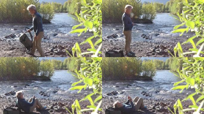 成熟的男性徒步旅行者在日出时在河滩上放松