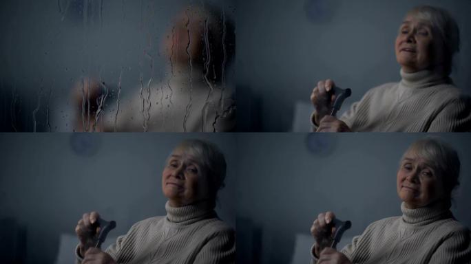 老人哭泣的女士独自坐在下雨的窗户后面的房间里，老年孤独