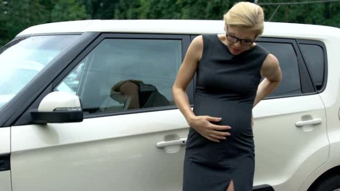 美丽的怀孕上班族走到她的汽车上，感到强烈的胃痛