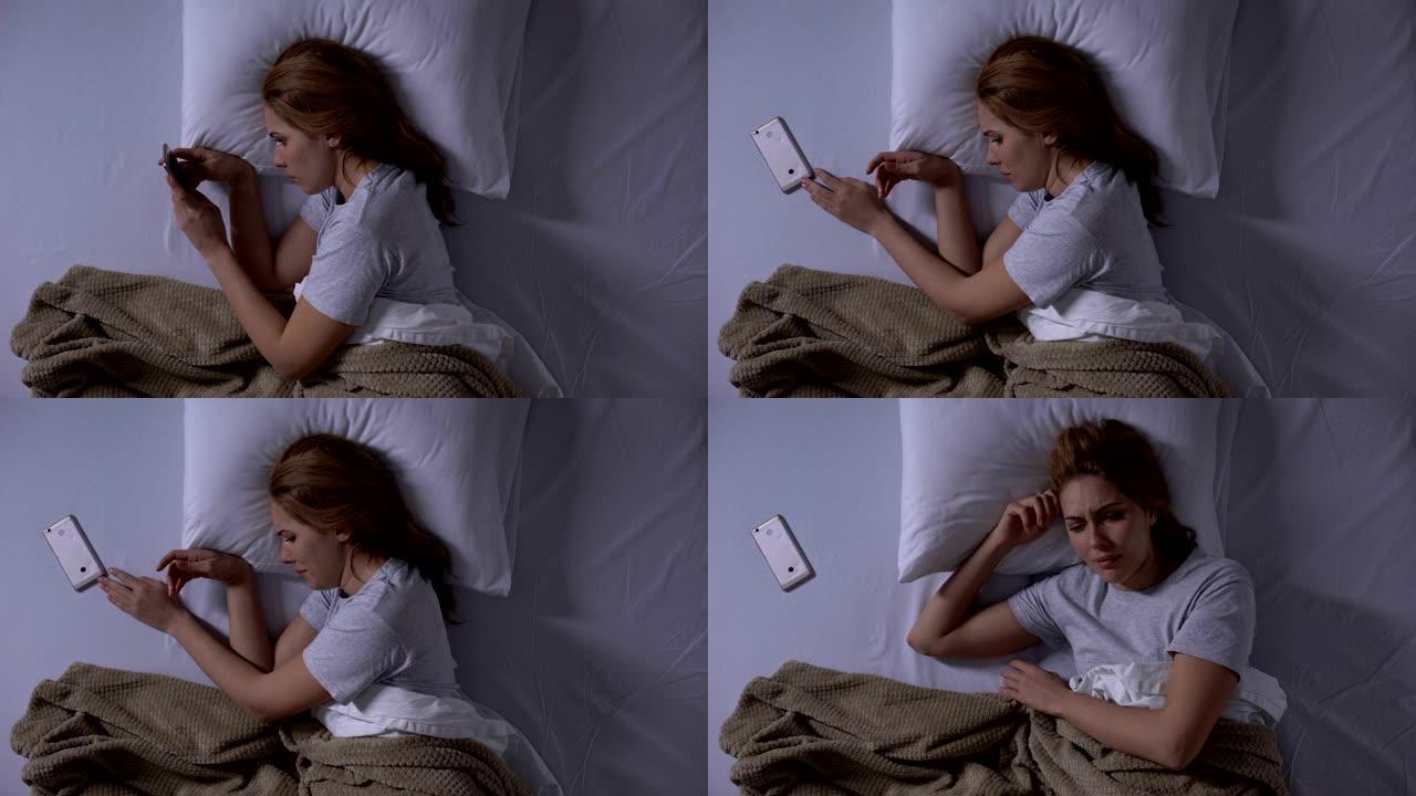 悲伤的女人哭着躺在床上的智能手机上阅读旧消息，回忆