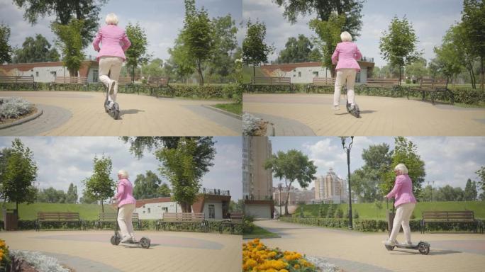 穿着粉色夹克的快乐可爱高级女子在公园骑马时使用踏板车。
