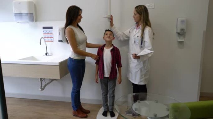 医生和妈妈站在小男孩旁边，而医生正在测量他的成长