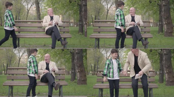 肖像可爱的爷爷和可爱的孙子坐在公园的长凳上，老人为男孩看书。