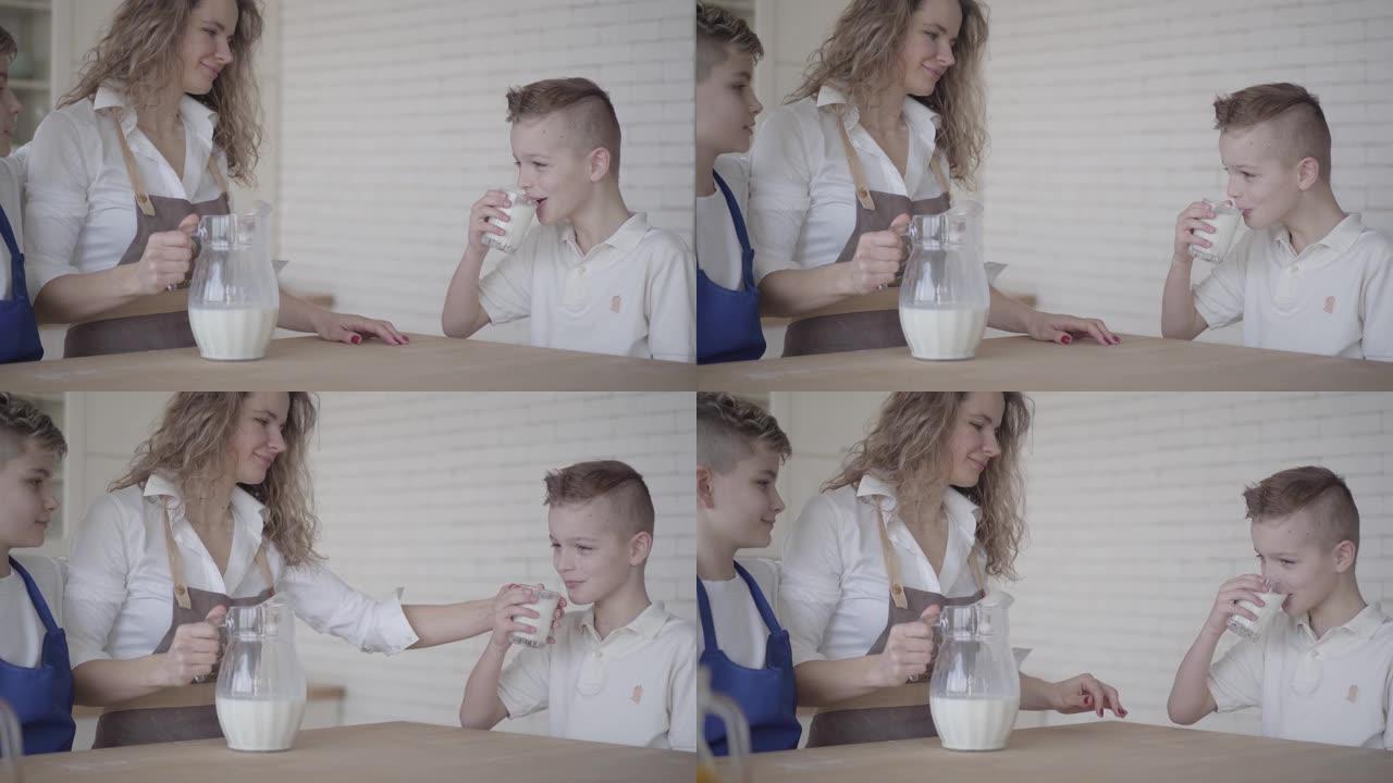 一个男孩坐在厨房里母亲和兄弟旁边的桌子旁喝牛奶。