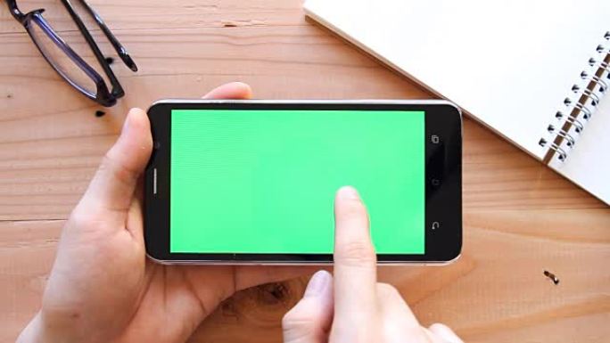 用手在木制办公室桌子上使用绿屏手机-顶视图