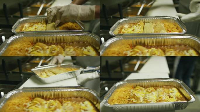 一个人在墨西哥餐厅的商业厨房里，将未包装的玉米粉蒸肉放入带有奶酪和米饭的金属烤盘中