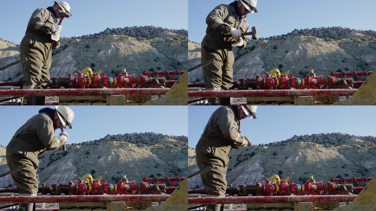 一个三十多岁的油田工人的慢动作镜头，在一个寒冷，阳光明媚的冬天的早晨，在石油和天然气钻井平台现场用锤