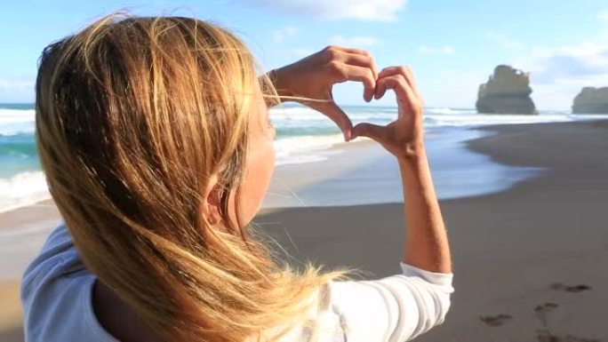年轻女子在海滩上制作心形手指框架