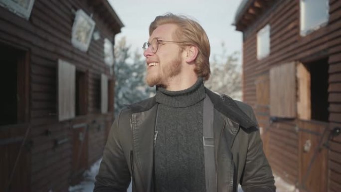 一个英俊的大胡子男人的肖像，戴着温暖的毛衣和敞开的夹克，戴着眼镜。