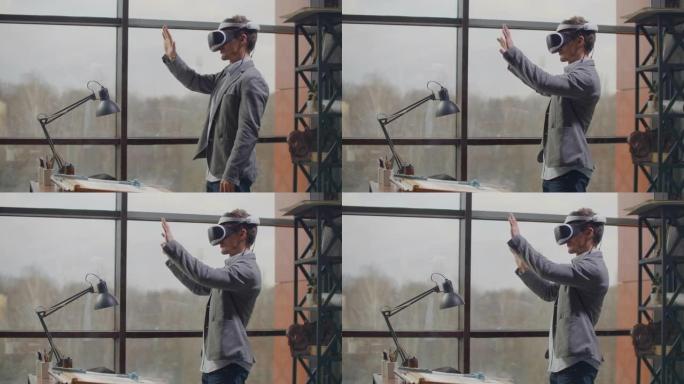 男工程师在大窗户附近的虚拟现实头盔中，用手模仿界面的工作。设计未来，虚拟架构和设计的概念，界面