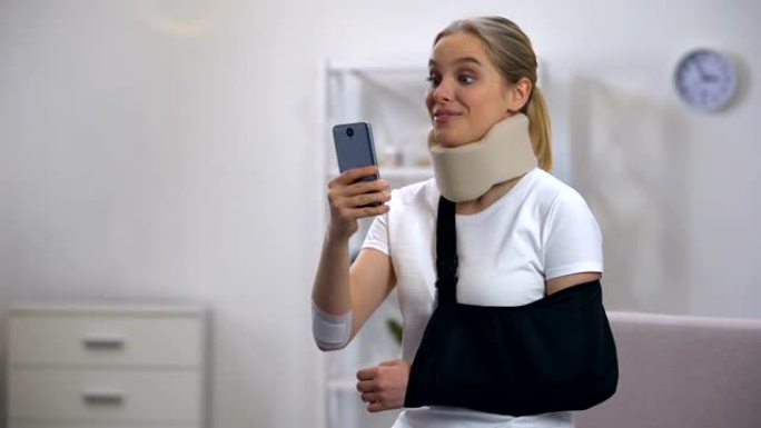 快乐的女人穿着泡沫颈圈和手臂吊带在手机康复中心聊天