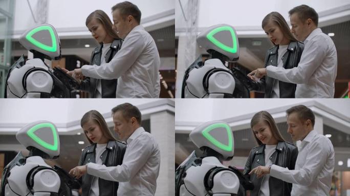 两人一男一女与机器人交流。用手在屏幕上按下机器人。在购物中心与一对夫妇互动的机器人助手。