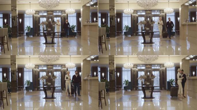 高加索男人和女人带着旅行包进入豪华酒店前厅并接近接待处的极宽镜头。富有的夫妇在高级住宿处登记入住。旅