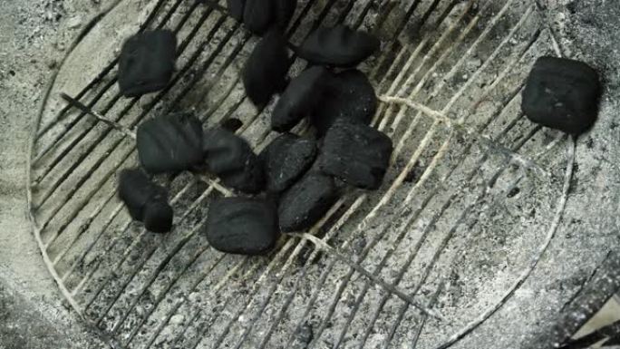 木炭煤块落在户外烧烤架上的金属炉排上，为烧烤做准备
