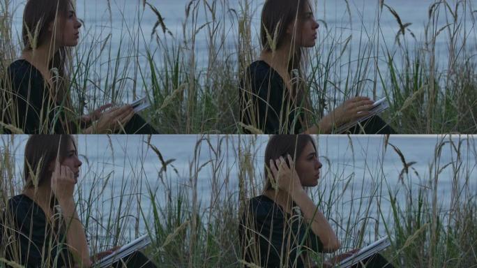 美丽的白人黑发女孩坐在湖边与书和看别处。享受户外宁静的美女。