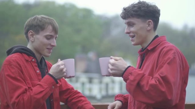 两个穿着红色夹克的男人用咖啡杯和微笑欢呼。朋友们在户外共度时光。人们快乐而微笑