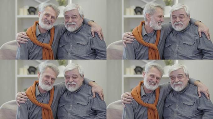 积极的白人老年男子拥抱、交谈和看着相机。最好的朋友在室内疗养院摆姿势的肖像。