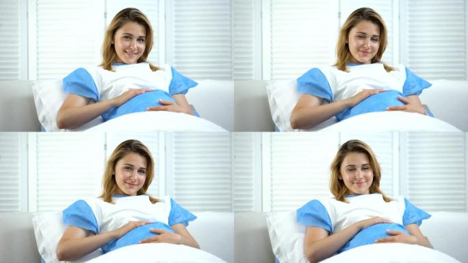 美丽孕妇抱着肚子对着镜头微笑，产前护理