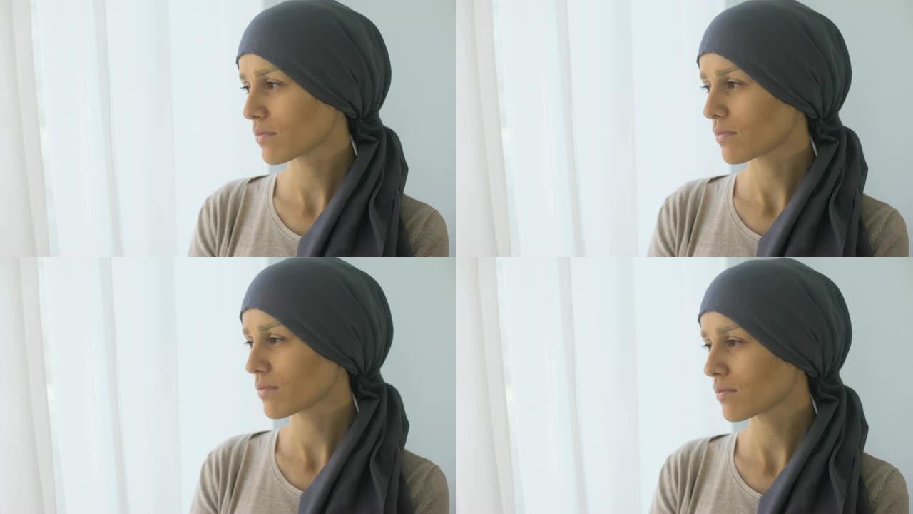 戴着头巾的沮丧女人看着窗户，康复中心，致命疾病