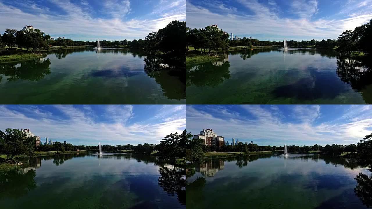 空中: 湖悬崖公园景观在水面附近飞行，令人惊叹的早晨反射，喷泉在空中高喷，达拉斯德克萨斯天际线在背景