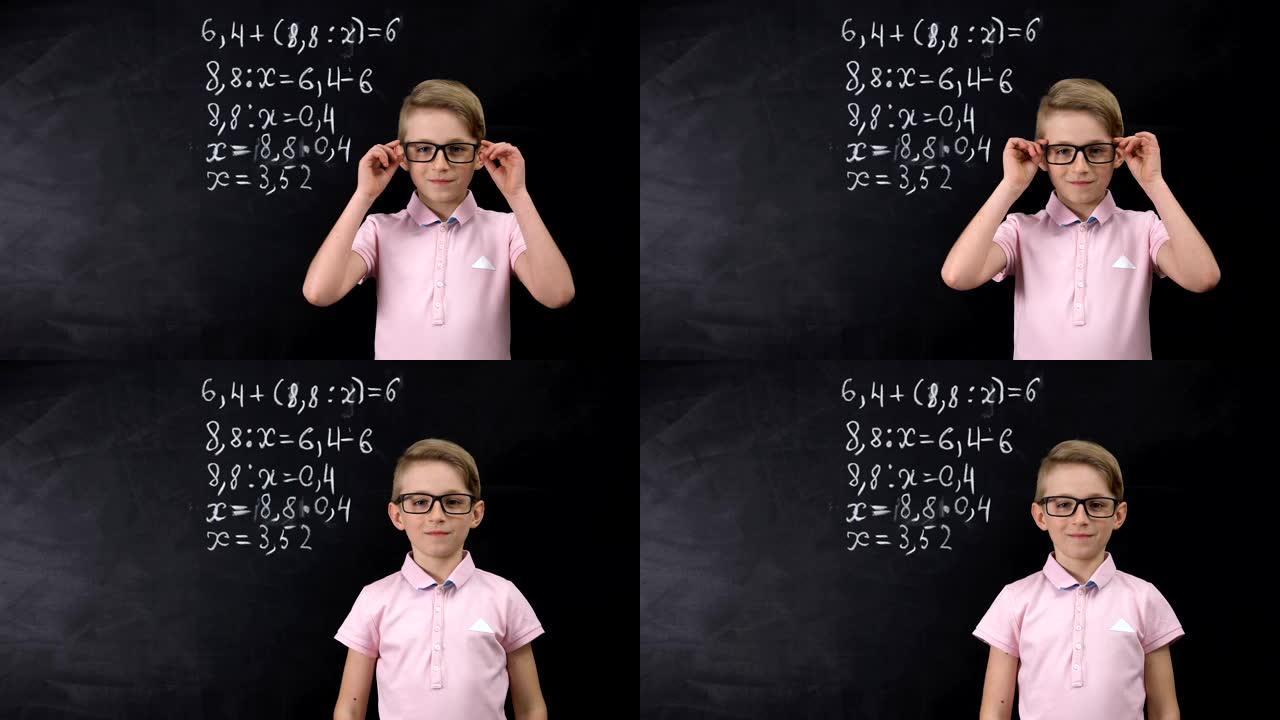 戴眼镜的可爱的书呆子男生站在黑板附近，写数学练习