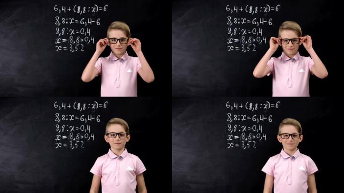 戴眼镜的可爱的书呆子男生站在黑板附近，写数学练习