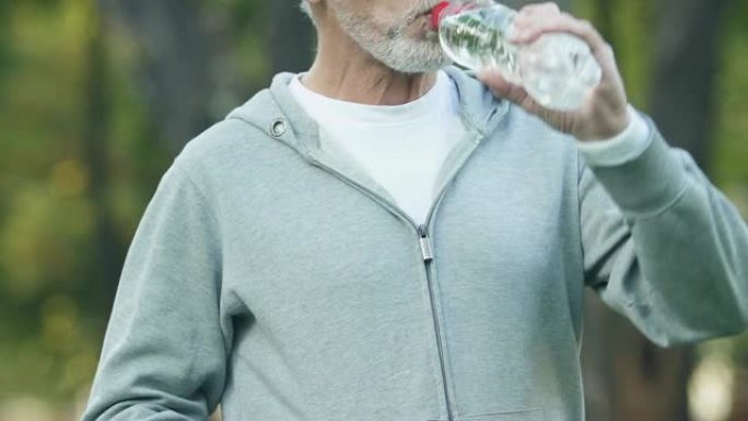 成熟的男人在镜头前摆姿势喝水，恢复矿物质的平衡