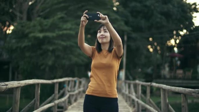 女人在木桥上用智能手机拍照