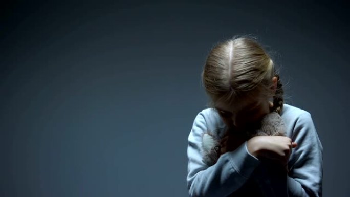 孤独的小孩拥抱泰迪熊，欺凌概念，黑暗的背景