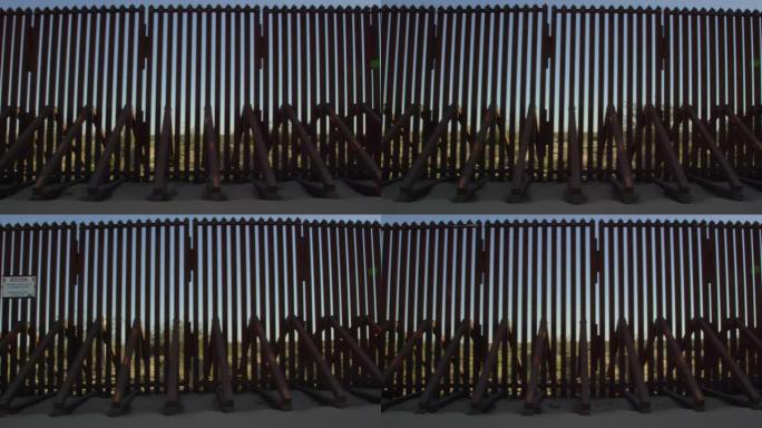 在阳光明媚的日子里，从墨西哥和美国之间的钢板条边界墙 (美国一侧) 的车辆侧面移动射击