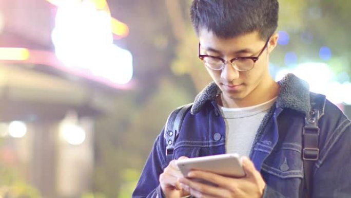 亚洲男子学生晚上在街上手持手机