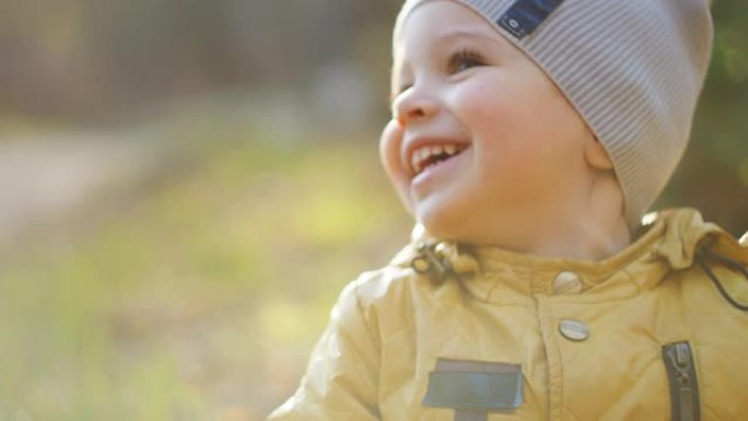 慢动作: 穿着黄色外套的小男孩坐在阳光下的森林中探索周围的世界。在林地里尽情享受和欢笑。自由快乐的童
