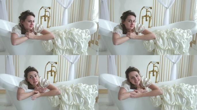 美丽有趣的年轻女子在球复古连衣裙躺在白色背景的白色浴室。