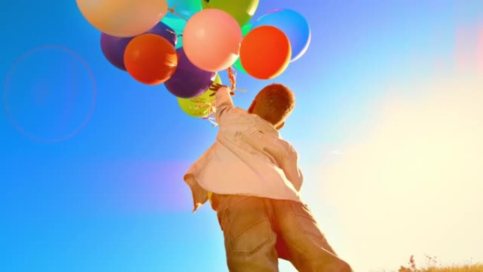 SLO MO Boy跳跃并向天空释放一堆彩色气球