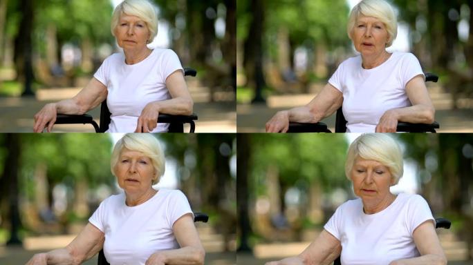 坐在轮椅上的悲伤女人深深叹息坐在户外，残疾，特写