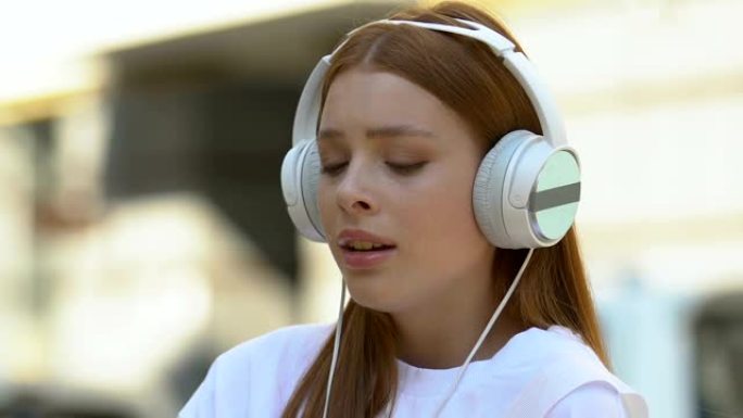 哭泣的女性青少年在户外戴着耳机听音乐变得多愁善感