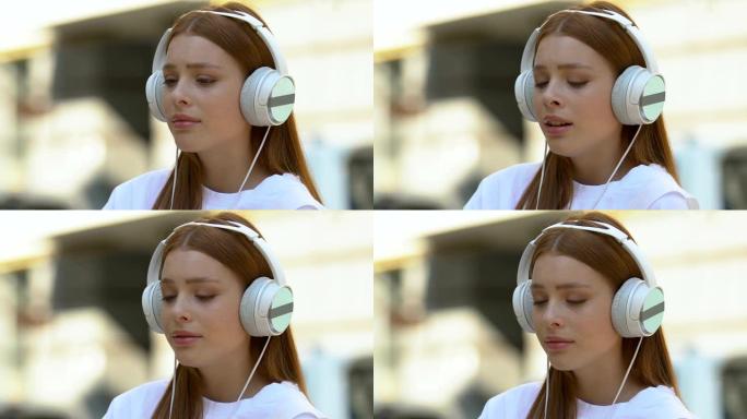 哭泣的女性青少年在户外戴着耳机听音乐变得多愁善感